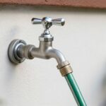 Kran ogrodowy zamontowany na elewacji domu z podłączonym wężem ogrodowym