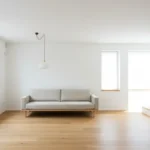Minimalistyczny salon z białymi ścianami, beżową sofą i drewnianą podłogą